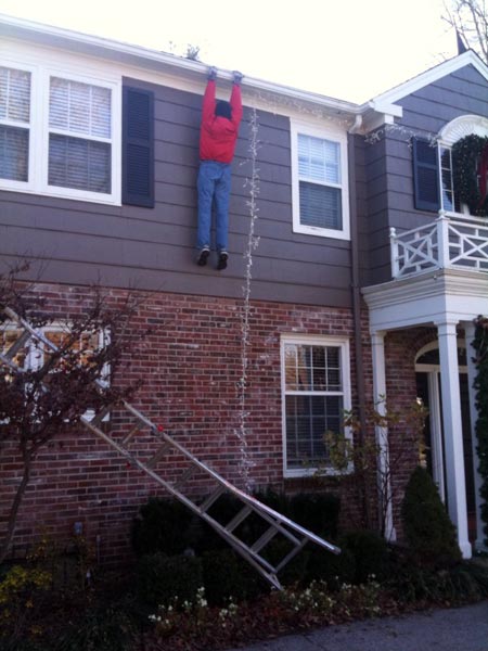 Man hanging from gutter with Christmas decorations